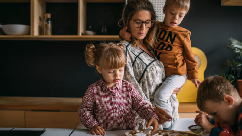 A woman and three children decorate biscuits in the kitchen.