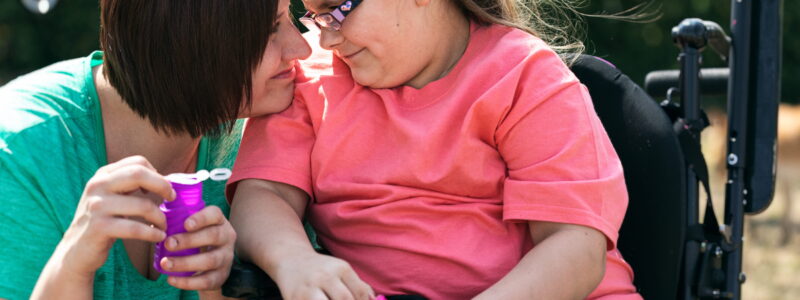 A woman and a girl who uses a wheelchair blow bubbles together