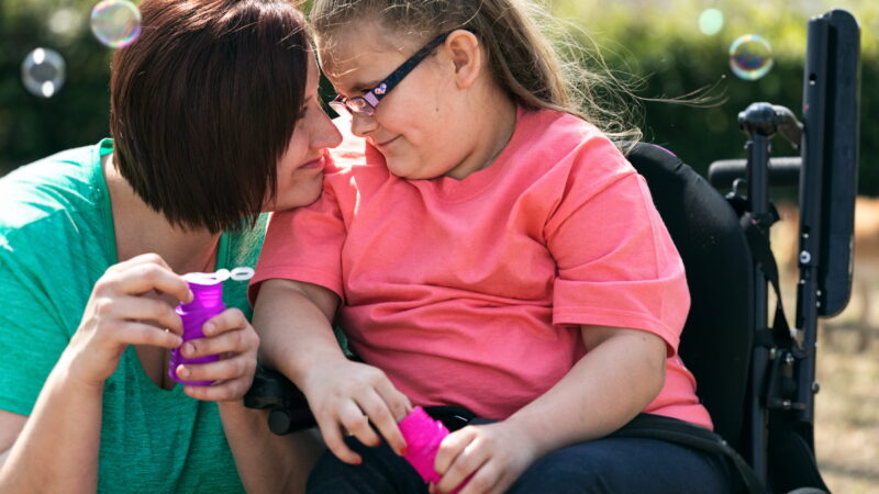 A woman and a girl who uses a wheelchair blow bubbles together