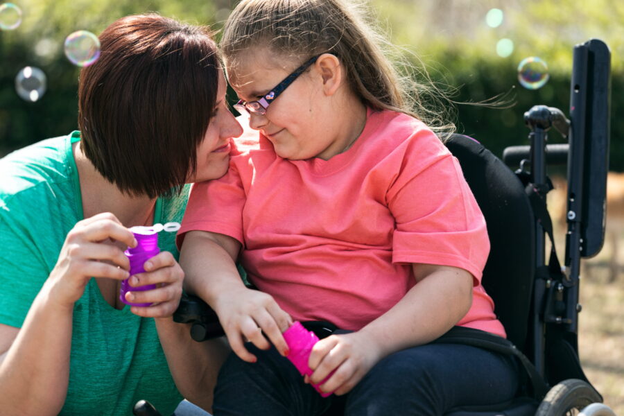 A woman and a girl who uses a wheelchair blow bubbles together
