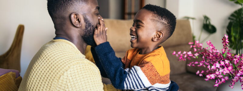 A man and a boy laugh together at home.