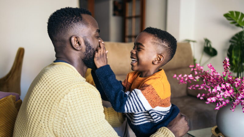 A man and a boy laugh together at home.