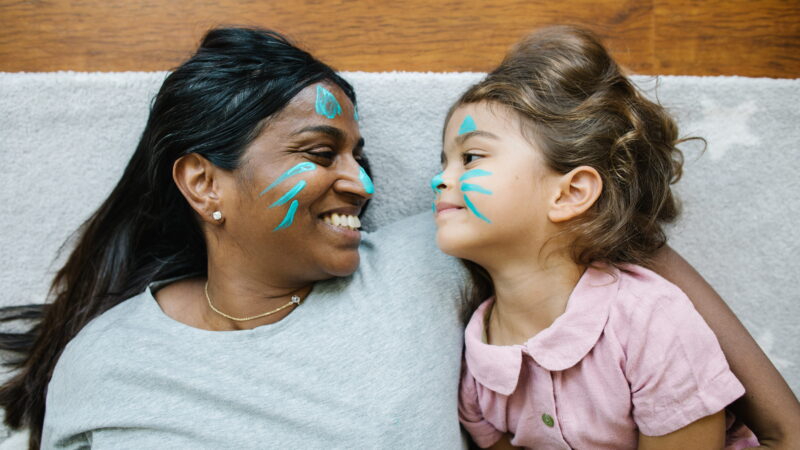 A woman and a girl lie together with matching face paint.