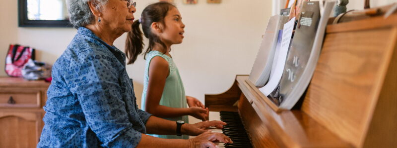 An older woman and a girl play piano together.