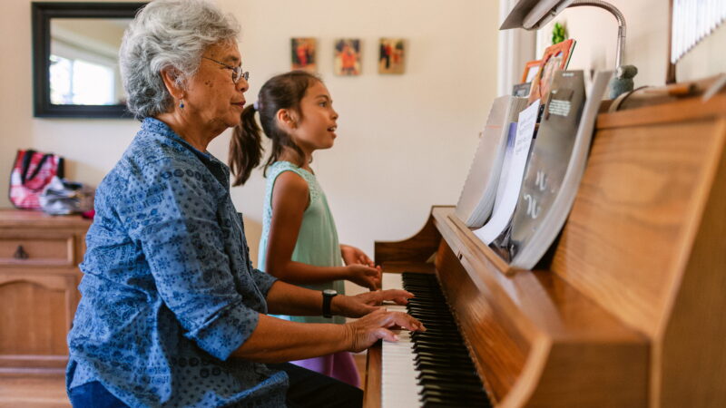 An older woman and a girl play piano together.